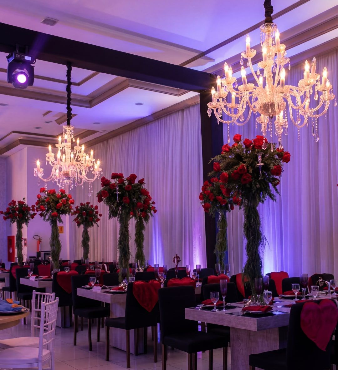 Salão do Espaço Belladata montado para festa de 15 anos, com lustres, rosas vermelhas e iluminação lilás