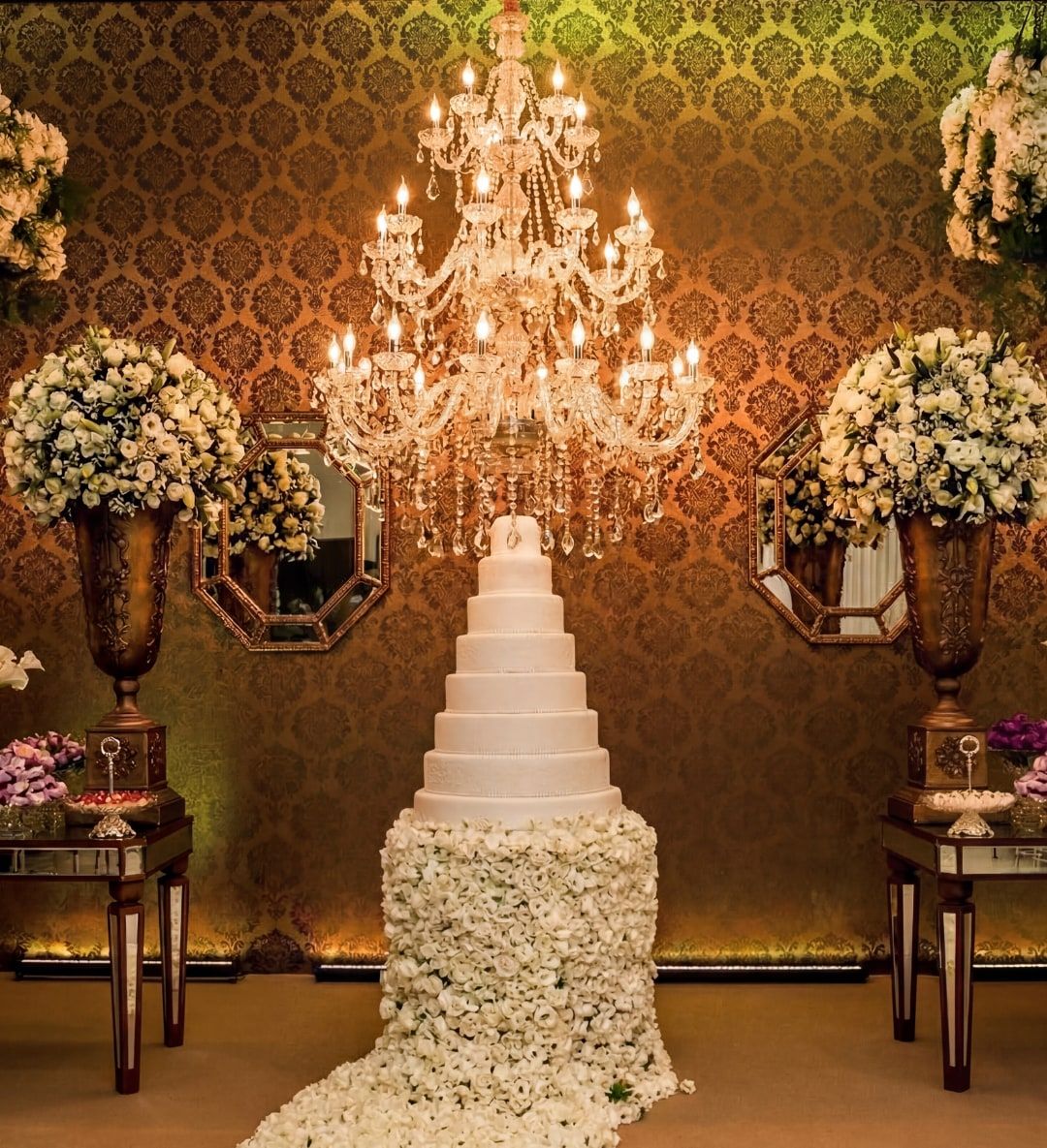 Bolo de casamento branco sob lustre de cristal, com tapete de flores