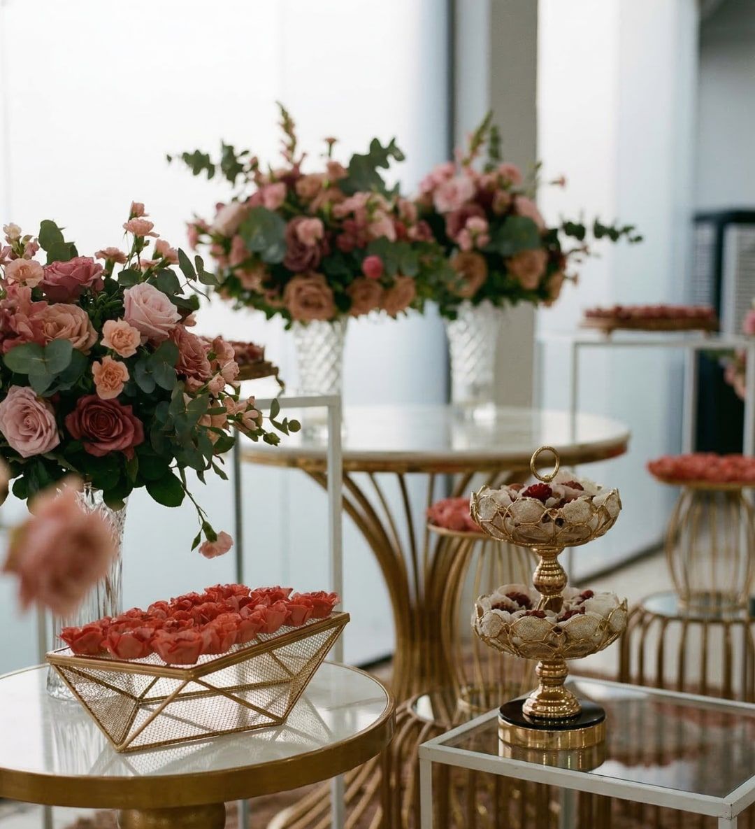 Mesa com arranjo alto de rosas e bandejas de doces